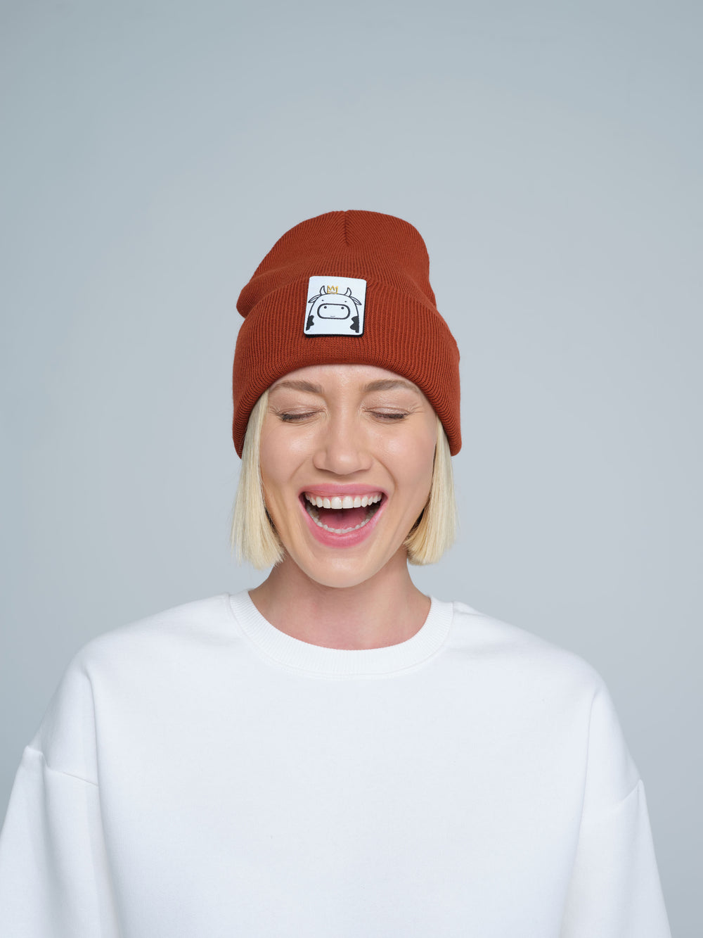 Person wearing a brick brown beanie with a logo on a plain background