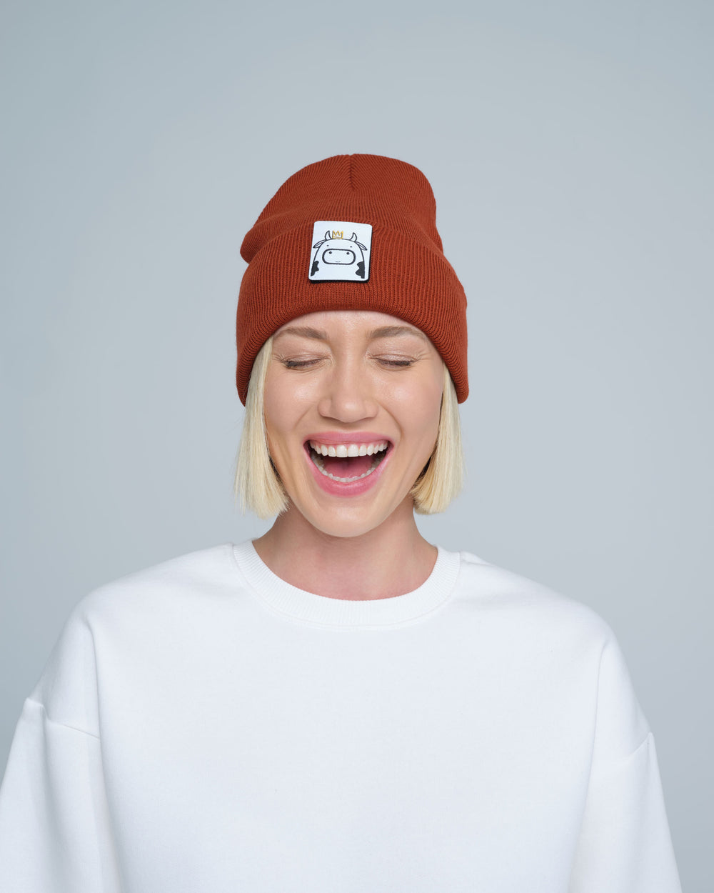 Person wearing a brick brown beanie with a logo on a plain background