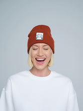 Person wearing a brick brown beanie with a logo on a plain background