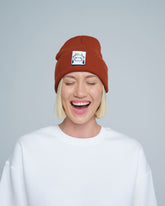 Person wearing a brick brown beanie with a logo on a plain background