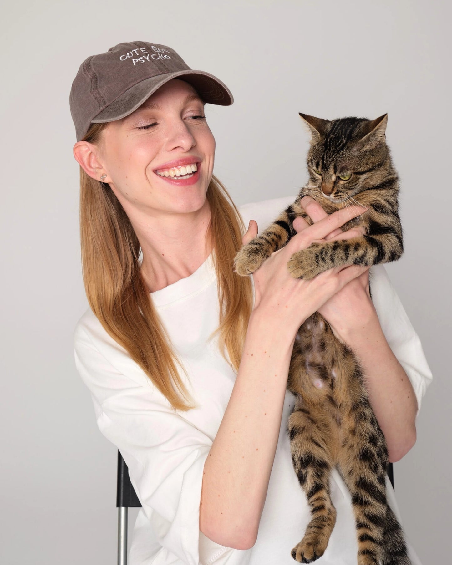 woman wearing Cute But Psycho Brown Washed Cap holds cat in her hands
