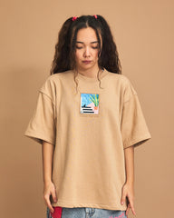 Person wearing a beige t-shirt with a graphic design on a brown background