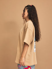 Person wearing a beige t-shirt with a colorful graphic on a brown background