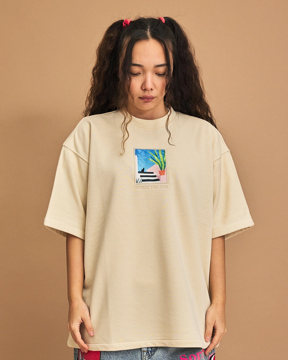 Person wearing a beige t-shirt with a colorful graphic on a brown background