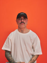 Man wearing a black cap and white t-shirt against an orange background