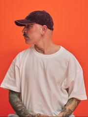 Person wearing a white t-shirt and dark cap against an orange background