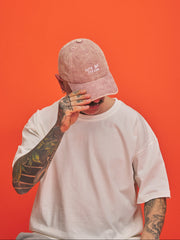 Person wearing a pink cap and white t-shirt against an orange background