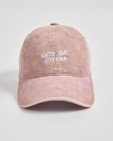 Pink corduroy cap with 'Cute But Psycho' text on a light gray background