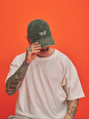 Person wearing a green corduroy cap with 'Cute But Psycho' text, covering their face against an orange background