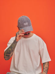 Person wearing a Cute But Psycho Stone Grey Corduroy Cap and white t-shirt against an orange background