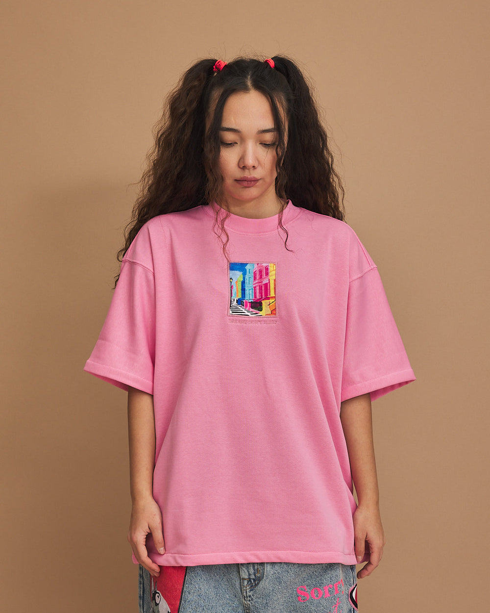 Person wearing a pink oversized t-shirt with a colorful graphic on a brown background