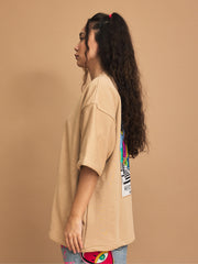 Woman wearing a beige oversized shirt with colorful designs on a brown background