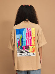 Person wearing a beige t-shirt with a colorful 'Notting Hill' graphic on the back against a brown background
