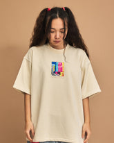 Person wearing a cream t-shirt with a colorful graphic on a brown background