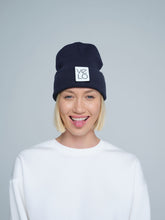 Person wearing a dusty navy beanie with a VELO logo on a gray background