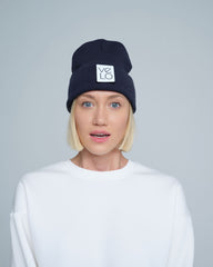 Person wearing a navy beanie with a logo on a gray background