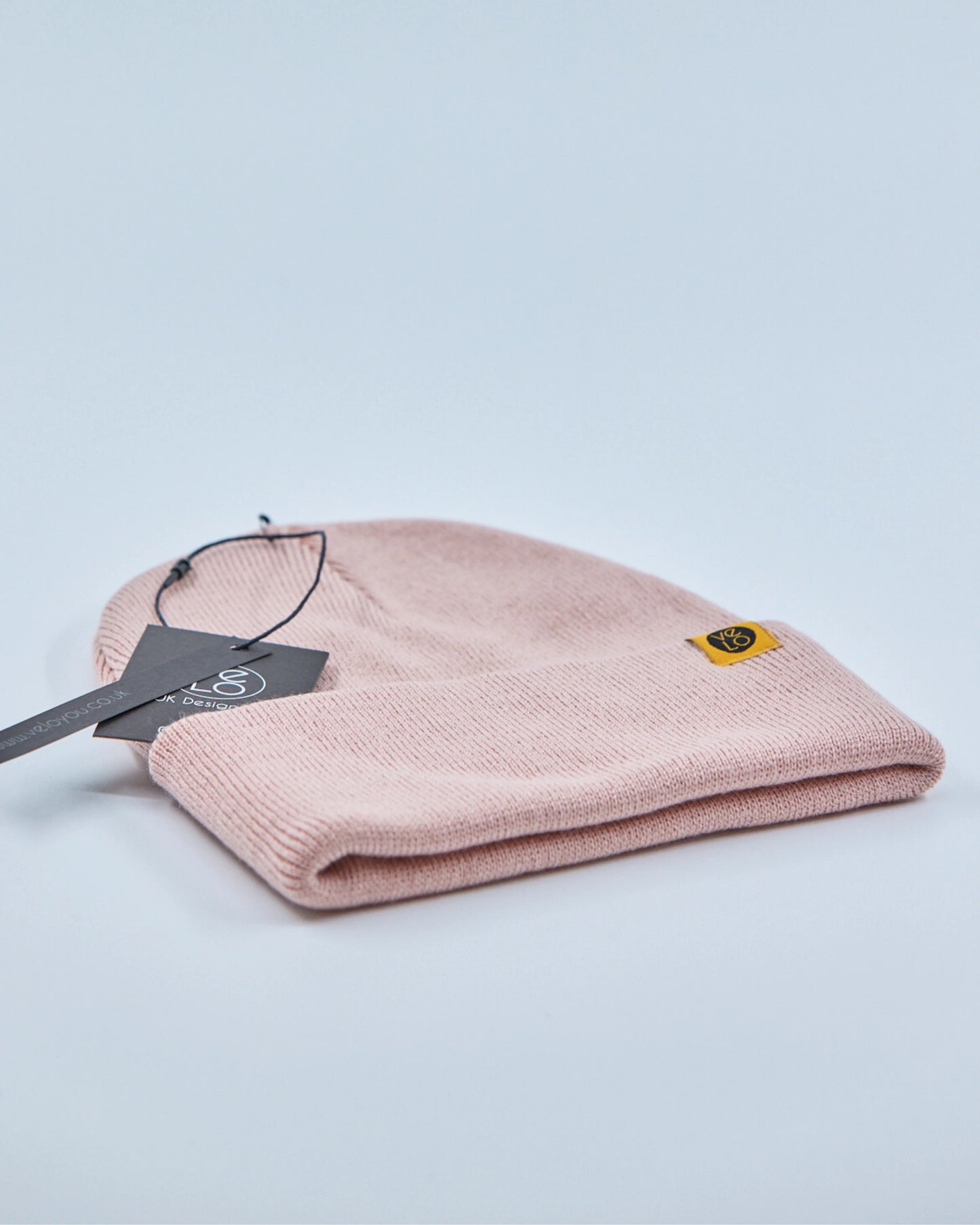 Dusty rose pink beanie with a tag on a light gray background