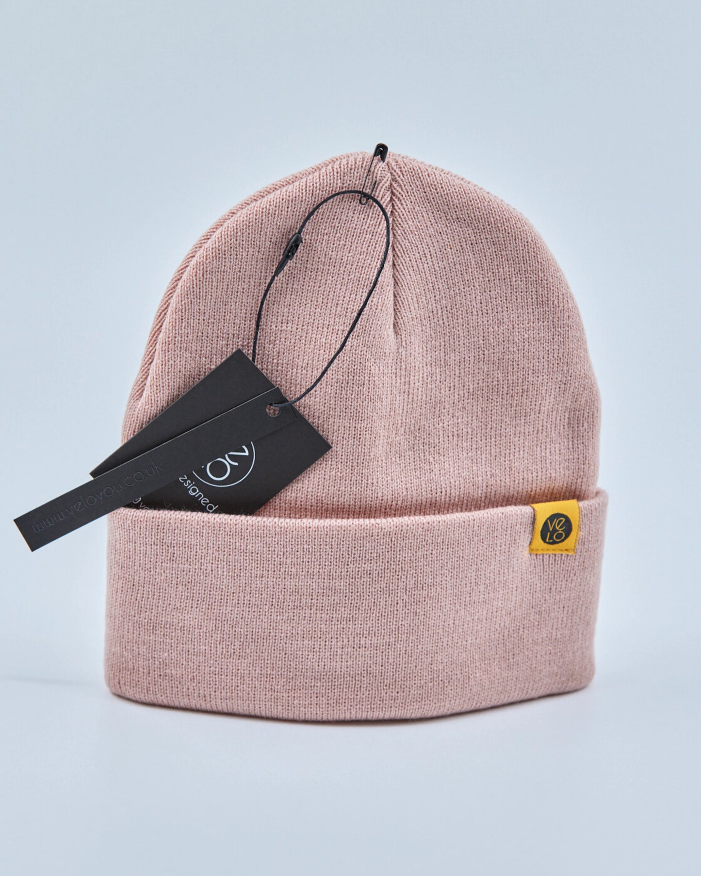 Dusty rose pink beanie with a brand tag on a light gray background
