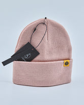 Dusty rose pink beanie with a brand tag on a light gray background