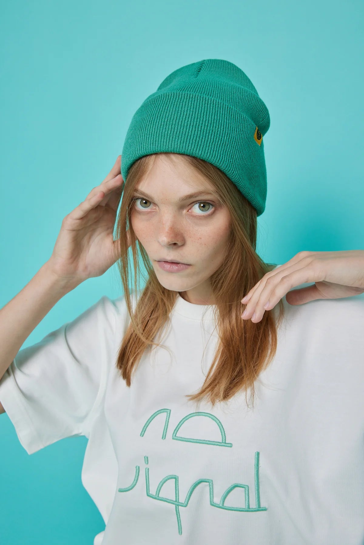 Person wearing a green beanie and white t-shirt with text against a teal background