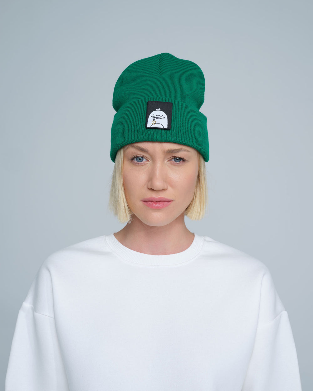 A person wearing green beanie with a duck patch on a gray background