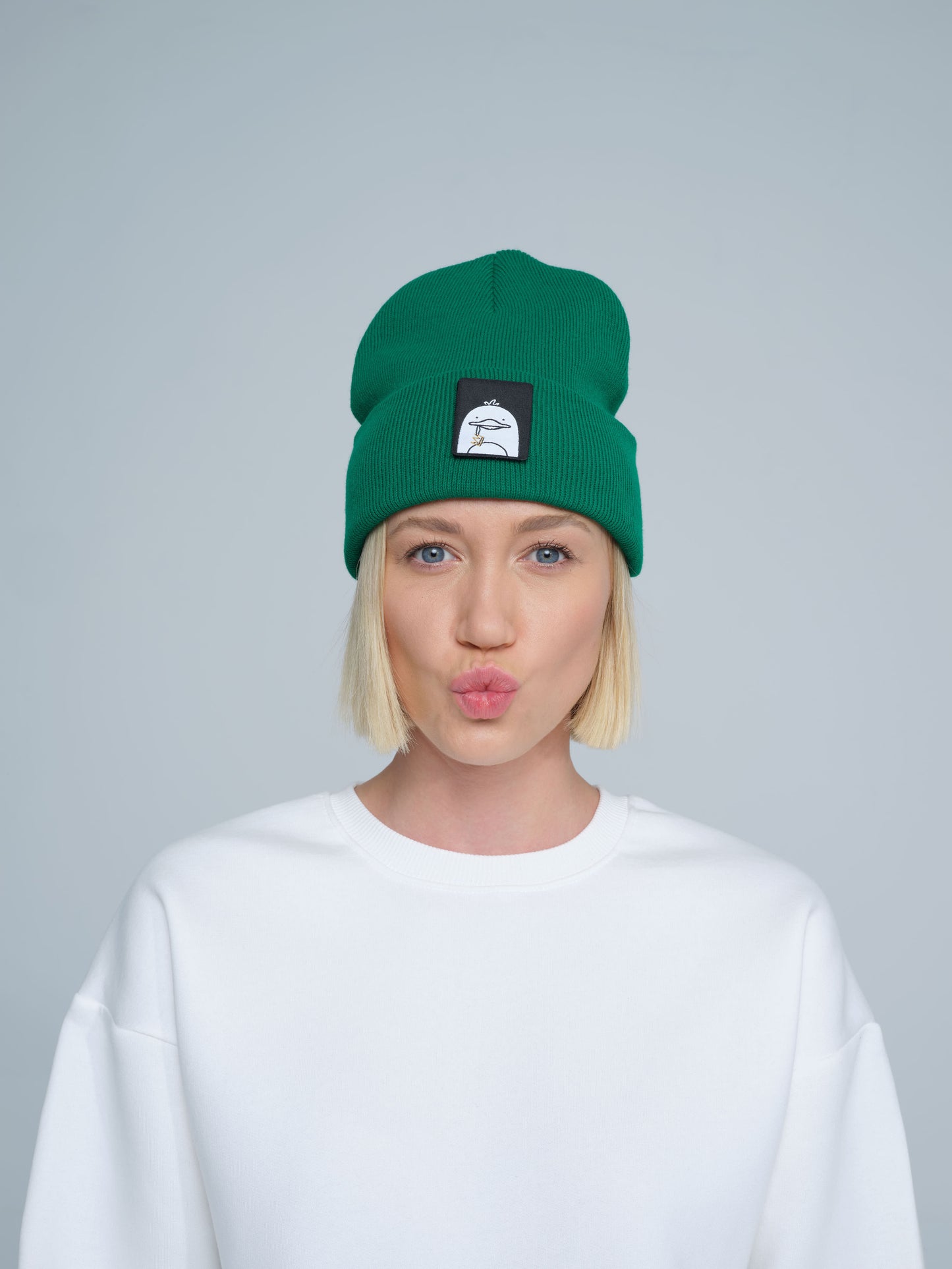 A person wearing green beanie with a duck patch on a gray background