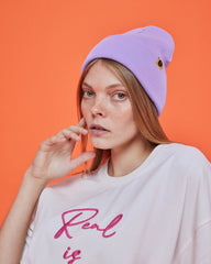 Person wearing a lilac purple beanie and white shirt with pink text against an orange background