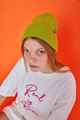 Person wearing a green beanie and white t-shirt with pink text on an orange background