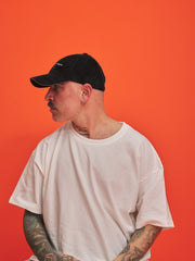 Man wearing a black cap and white t-shirt against an orange background