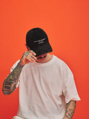Person wearing a black cap and white t-shirt against an orange background