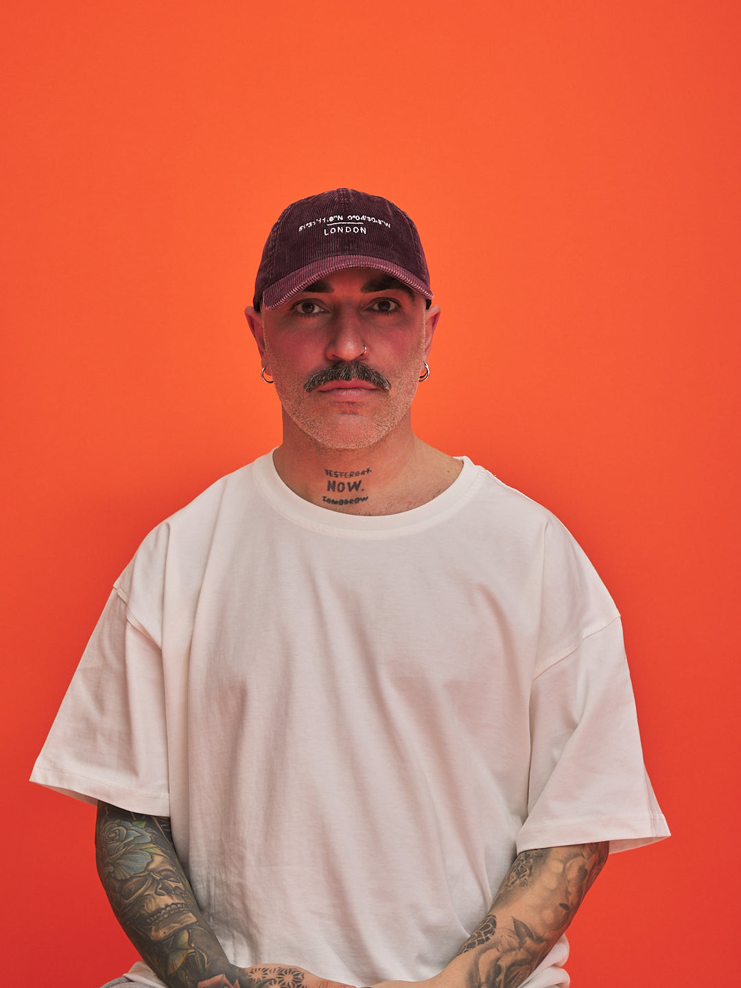 Man wearing a white t-shirt and dark cap against an orange background