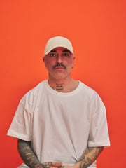 Man wearing a cream cap and t-shirt against an orange background