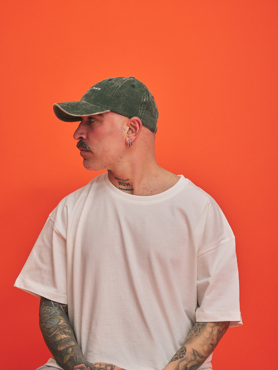 Man wearing a green cap and white t-shirt against an orange background