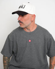side look of man wearing a gray t-shirt with a small red logo and a white baseball cap with an black brim and Arabic 'love' text on a plain background.