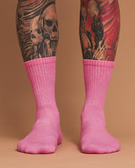 Person wearing pink socks with tattooed legs on a brown background