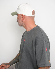 Man wearing a gray t-shirt with small logos on a white background and shows adjustable flip tag of the cap
