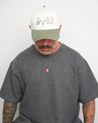 Man wearing a gray t-shirt with a red 'VELO' logo and a white cap with safe green brim and Arabic 'LOVE' text.