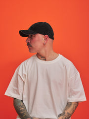 Person wearing a black cap and white t-shirt against an orange background