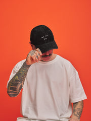 Person wearing a black cap with text and a white t-shirt against an orange background