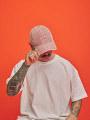 Person wearing a pink cap and white t-shirt against an orange background