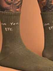close up of khaki socks with text 'love you, BYE' worn by a person on a brown background