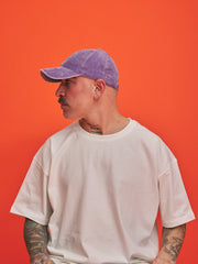 Person wearing a purple cap and white t-shirt against an orange background