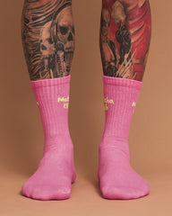 Pink socks with yellow text worn by a person with tattoos on a brown background
