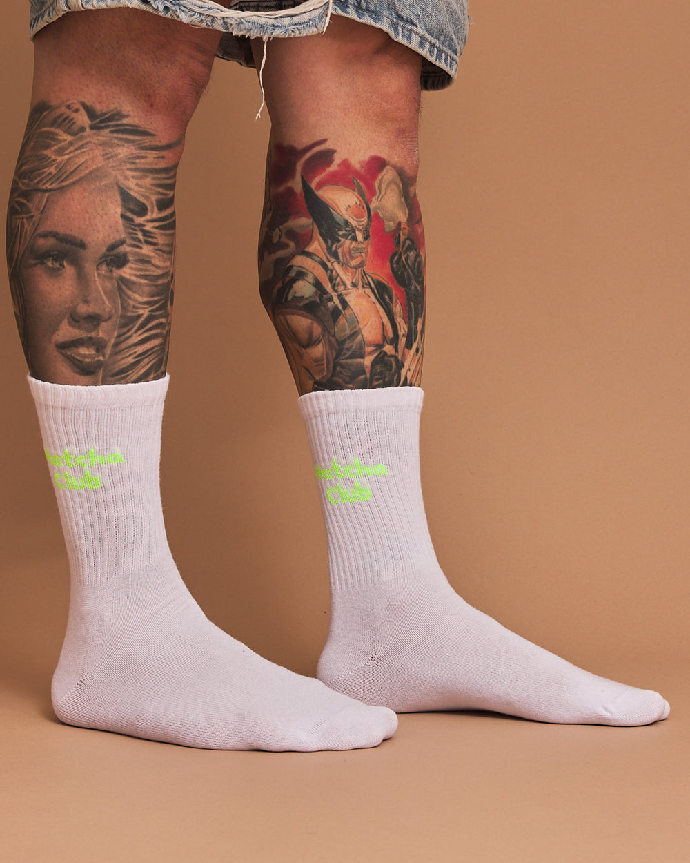 White socks with neon yellow text worn by a person with tattoos on a brown background