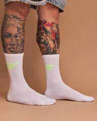 White socks with neon yellow text worn by a person with tattoos on a brown background