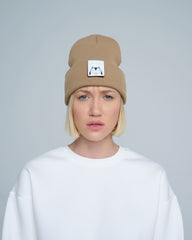 A person wearing mink brown colour beanie with cat illustration patch on the front