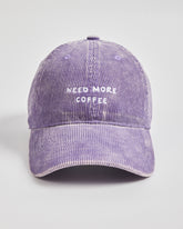 Purple corduroy cap with 'Need More Coffee' text on a light gray background