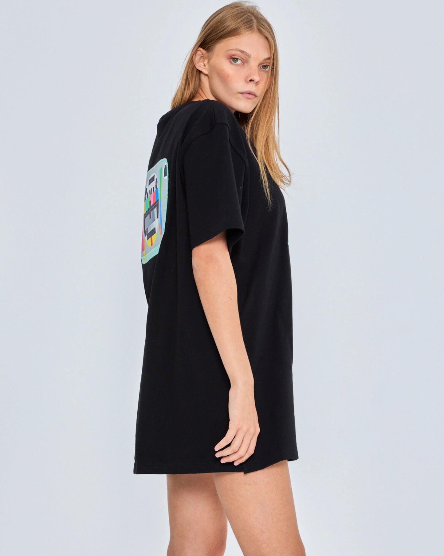 Woman wearing a black oversized t-shirt with a colorful graphic on the back against a light gray background