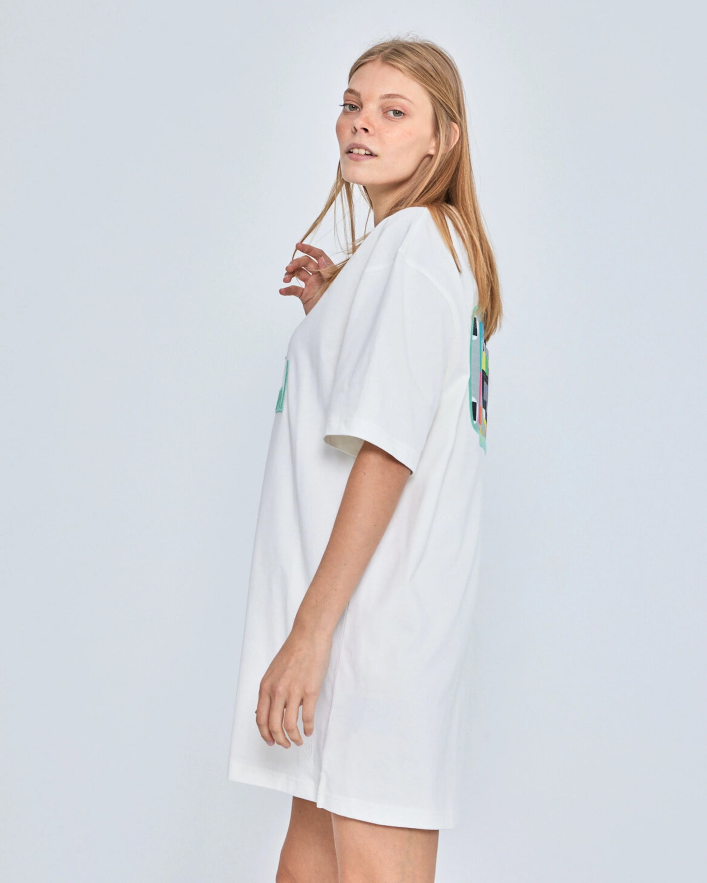 Woman wearing a white dress with colorful patterns on a plain background