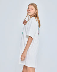 Woman wearing a white dress with colorful patterns on a plain background
